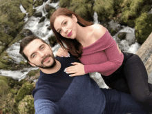 a man and a woman are posing for a photo in front of a waterfall