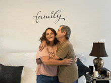 a man and woman hugging in front of a wall that has the word family written on it