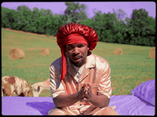 a man in pajamas and a red hat sits on a bed in front of a field of hay bales