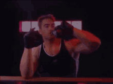 a man wearing boxing gloves and a black tank top is drinking from a bottle .