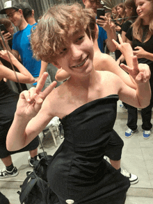 a boy in a black dress giving the peace sign