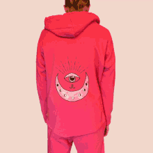 a woman is wearing a pink hoodie with an eye and a crescent moon on it