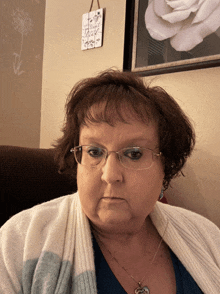 a woman wearing glasses is sitting in front of a picture of a rose and a sign that says " trust your heart "