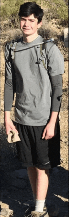 a young man wearing a grey shirt and black shorts with a backpack