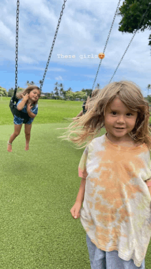 a little girl is standing in front of a swing with the words " these girls " written on it