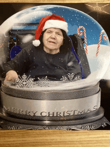 an elderly woman wearing a santa hat is in a snow globe with the words merry christmas on it