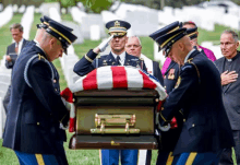 a group of men in military uniforms carrying a coffin in a cemetery