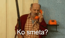 an older man is holding a gun and talking on a telephone .