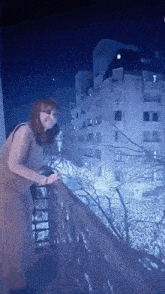 a woman in a mask is standing on a balcony at night looking out over a city .