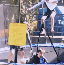 a group of people are playing on a trampoline with a yellow sign in the background that says warning .