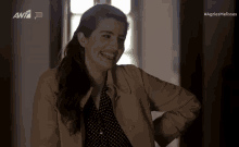 a woman in a trench coat is smiling in front of a screen that says ant7