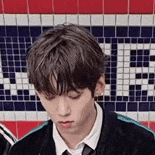 a young man in a suit and tie is sitting in front of a red , white , and blue tiled wall .