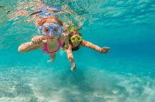 a woman and child are swimming underwater in the ocean .