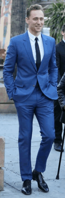 a man in a blue suit and black tie is standing on a sidewalk