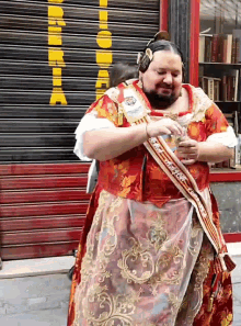 a woman in a red and gold dress has a sash around her waist that says ' feliz dia de la mujer ' on it