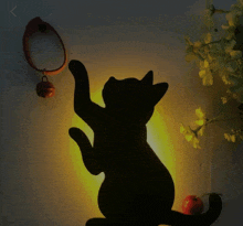 a silhouette of a cat reaching for something with a bell hanging from it