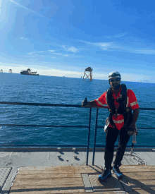 a man wearing a helmet and sunglasses stands on a deck overlooking a body of water