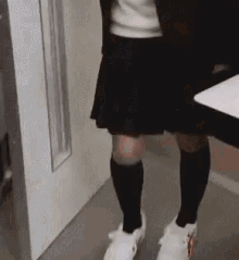 a woman wearing knee high socks and white sneakers is walking down a hallway .