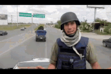 a man wearing a helmet and vest stands in front of a highway with a sign that says " mexico " on it