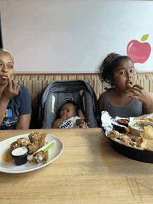 a baby in a stroller sits at a table with two women eating