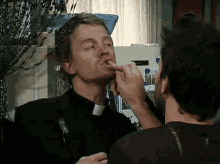 a man in a clergy collar is licking another man 's nose