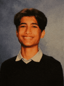 a young man wearing a black sweater and a white shirt smiles for the camera