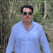 a man wearing sunglasses and a white shirt is standing in a forest