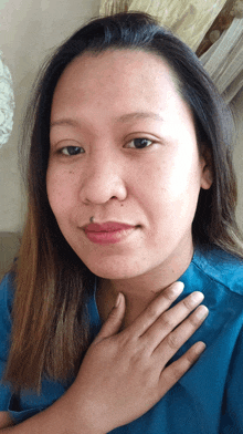 a woman wearing a blue shirt has her hand on her neck