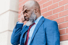 a man in a suit and tie is leaning against a brick wall and covering his face with his hand