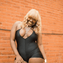 a woman wearing a black swimsuit and sunglasses is smiling in front of a brick wall