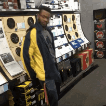 a man in a yellow jacket is standing in front of a wall of speakers and boxes that say sub