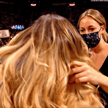 a woman wearing a mask holds another woman 's hair in front of a sign that says nba on it