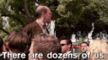 a group of people are standing in a park with the words `` there are dozens of us '' written above them .