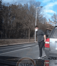 a man is standing on the side of the road next to a car with a stop sign in the background