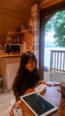 a little girl is sitting at a table with a tablet