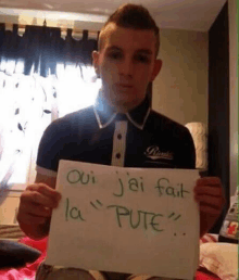 a young man is holding up a sign that says `` oui j'ai fait la pute '' .