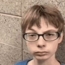 a young boy wearing glasses is making a funny face while standing in front of a brick wall .