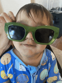 a baby wearing green sunglasses and a blue pajama top