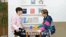 two young men are sitting at a table in front of a shelf with books on it including one about london