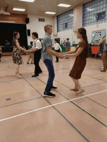 a group of people are dancing in a gym with a sign on the wall that says ' basketball ' on it