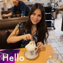 a woman sitting at a table with a cup of hot chocolate and the word hello written on the table