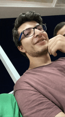 a young man wearing glasses and a maroon shirt smiles