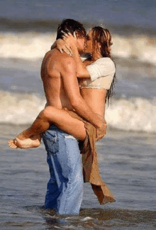 a man is holding a woman in his arms while they kiss on the beach .