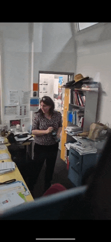 a woman in a floral shirt is standing in a cluttered room