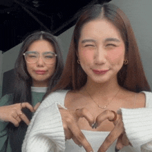 two women are making a heart shape with their fingers