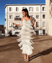 a woman wearing a white dress with fringe is standing on a sidewalk