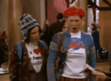 a woman wearing a shirt that says i love france is standing next to another woman wearing a hat .