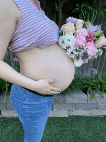 a pregnant woman is holding a bouquet of pink and white flowers on her belly