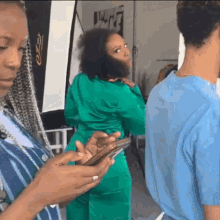 a woman in a green suit looks at her phone while standing next to a man in a blue shirt