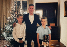 a man in a suit stands next to two boys in front of a christmas tree